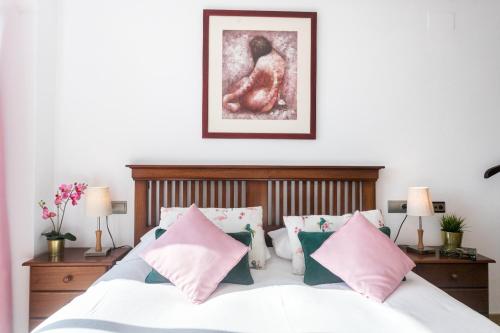 ein Schlafzimmer mit einem weißen Bett mit rosa und grünen Kissen in der Unterkunft Bungalow Altea junto al casco antiguo, piscina y barbacoa in Altea