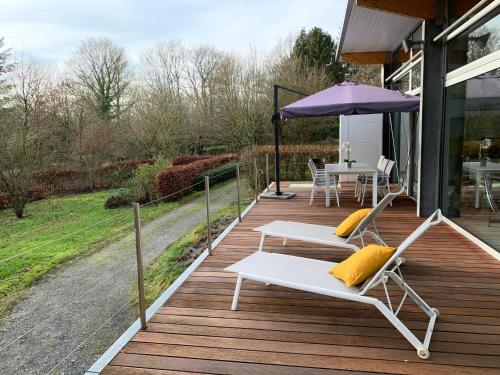 a deck with a table and chairs and an umbrella at La Maison d'Architecte en pleine nature - le "Clos des Chevreuils" in Barbençon