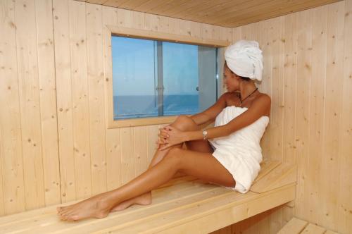 Eine Frau sitzt in einer Sauna in der Unterkunft Hotel Atlantico in Lido di Jesolo