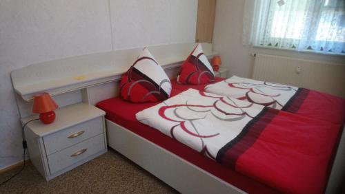 ein kleines Schlafzimmer mit einem Bett mit roten und weißen Kissen in der Unterkunft Ferienwohnung Ehrenfriedersdorf in Ehrenfriedersdorf