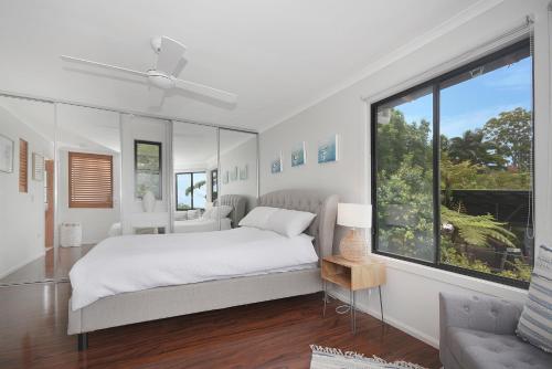 a white bedroom with a bed and a large window at Tree Top Oasis in Buderim