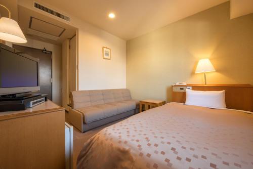 Pacific Hotel Shiroishi في Shiroishi: غرفه فندقيه بسرير واريكه