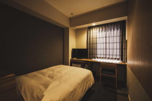 a bedroom with a bed and a desk and a window at Hotel Kajiwara in Matsuyama