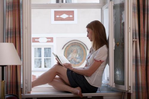 a woman sitting in a window reading a book at Posthotel Kolberbräu in Bad Tölz