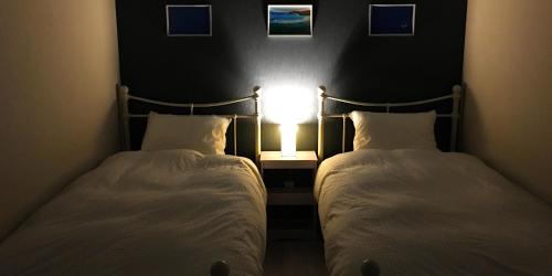 two beds in a room with a light on the wall at SOU東恩納 in Uruma