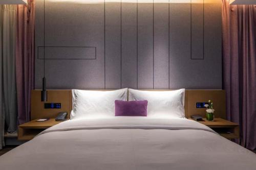 a large white bed with a purple pillow on it at Mercure Kunshan Hi Tech Zone in Kunshan