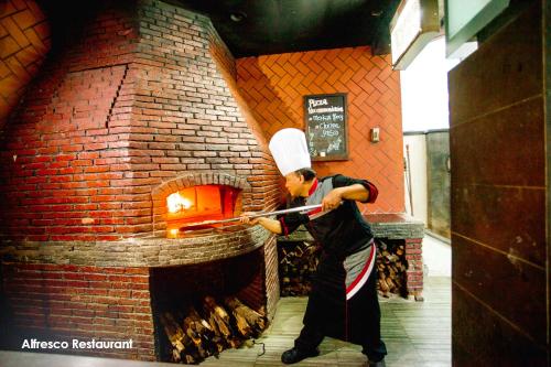 a man in a chefs hat is putting something into a brick oven at Menara Peninsula Hotel in Jakarta