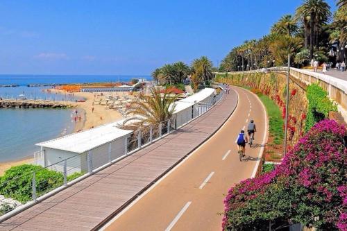Dos personas andando en bicicleta por una calle junto a una playa. en Casa Dede, en San Remo