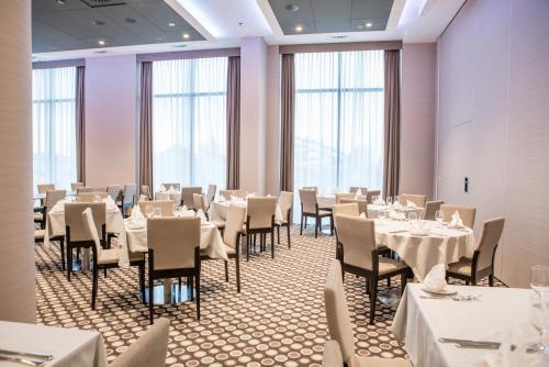 a restaurant with white tables and chairs and windows at Holiday Inn Dąbrowa Górnicza-Katowice by IHG in Dąbrowa Górnicza
