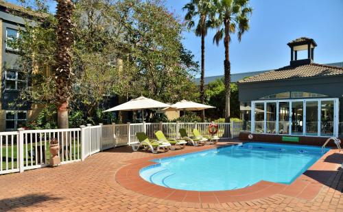 a pool with chairs and umbrellas next to a building at Holiday Inn Johannesburg OR Tambo Airport Hotel by IHG in Kempton Park