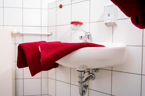 baño con lavabo blanco y toalla roja en Wohlfühlhotel IM SCHLOSSPARK - Self CheckIn en Willebadessen