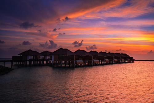 a pier with huts on the water at sunset at VARU by Atmosphere - Premium All Inclusive with Free Transfers in North Male Atoll