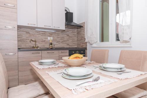 a table with plates and a bowl of fruit on it at Modern Apartment Baćo with Jacuzzi in Šibenik