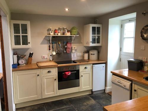 a kitchen with white cabinets and a stove top oven at Charming cottage with loch and hill views nr Edinburgh in Cobbinshaw