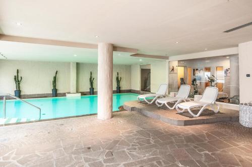 a swimming pool with white chairs and a swimming pool at Adler ApartHotel in Moena