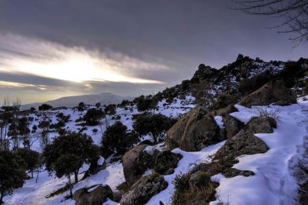a snow covered hill with rocks and trees and the sun at Hotel Sara De Ur in La Cabrera