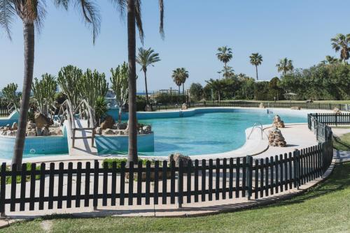 einen Pool in einem Resort mit Palmen und einem Zaun in der Unterkunft Apartamento Roller - a pie de playa in Zahara de los Atunes