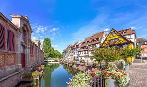 a canal in a city with buildings and flowers at Hôtel Au Vieux Moulin in Lapoutroie