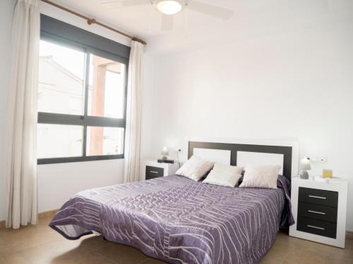 a bedroom with a bed with a purple comforter and a window at Apartamentos Atenea Playa Romana in Alcossebre