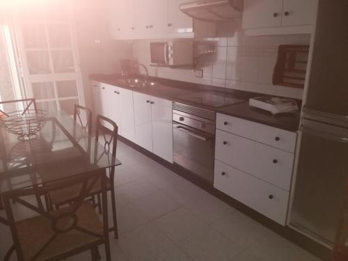 een keuken met witte kasten en een tafel met stoelen bij Piso de Verano in O Grove