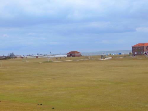 a large grass field with a building and the ocean at Deichkrone in Horumersiel
