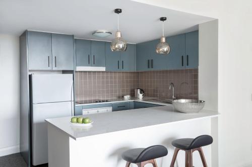 a kitchen with blue cabinets and two stools at Mantra Chatswood in Sydney