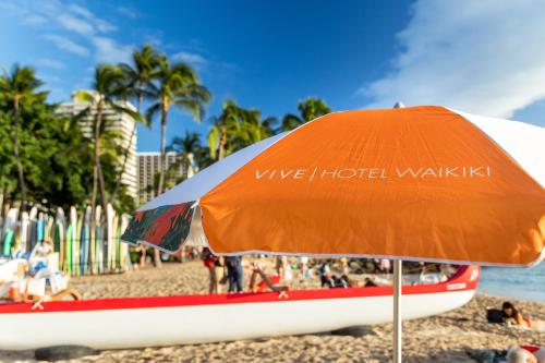 an orange umbrella and a boat on a beach at VIVE Hotel Waikiki in Honolulu