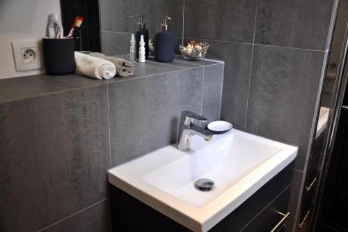 La salle de bains est pourvue d'un lavabo blanc et d'un mur gris. dans l'établissement Charming Apartment In Boulogne, à Boulogne-Billancourt
