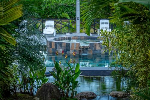 una piscina en un jardín con 2 sillas de césped en Residencias Arenal, en Fortuna