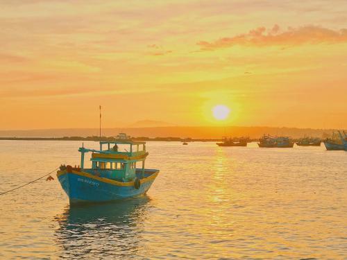 ein blaues Boot im Wasser bei Sonnenuntergang in der Unterkunft Hotel Khanh An in Phan Thiet