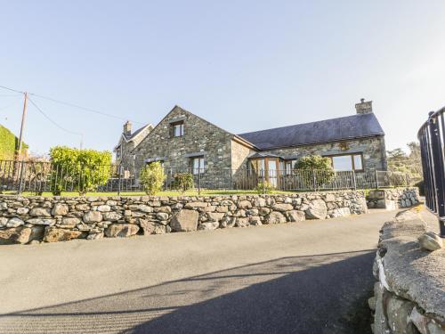 a stone house with a stone wall and a fence at Awel Y Llan in Llanfair