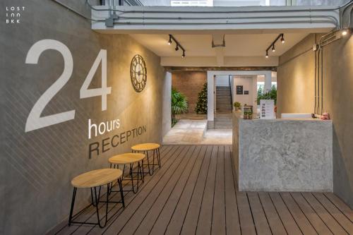 a group of stools against a wall with a sign that reads hours reception at Lost Inn BKK in Bangkok