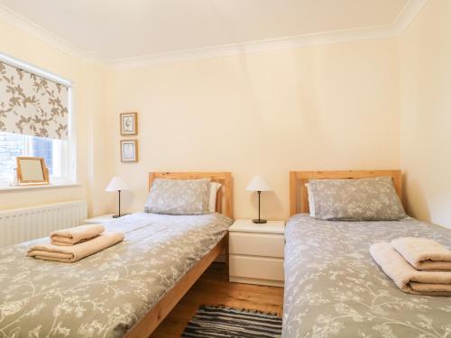 two beds in a bedroom with two lamps and a window at Siskin in Keswick