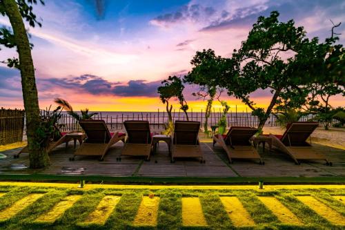 a group of chairs and a table on a deck with a sunset at Veena - By the Beach in Mararikulam