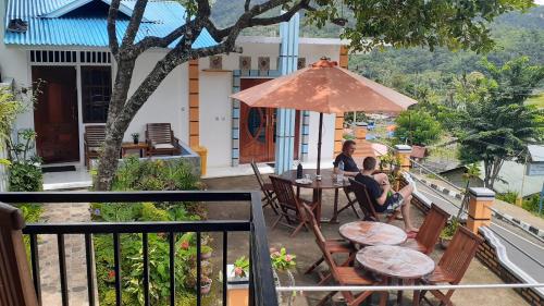 a woman sitting at a table with an umbrella on a balcony at Bintang Bungalow Tour & Travel in Kelimutu