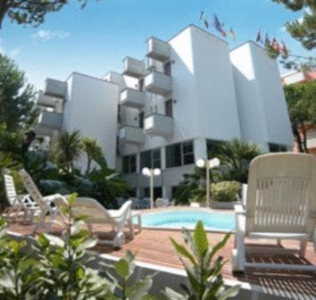 a large building with a pool and chairs in front of it at Hotel Kiss in Cesenatico