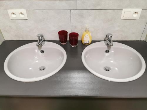 two white sinks in a bathroom with two red glasses at Hôtel Belair "Ravel Etape" in Waimes