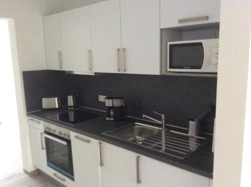 cocina con armarios blancos, fregadero y microondas en Ferienwohnung 2, Wildes Wässerchen, en Bad Hersfeld