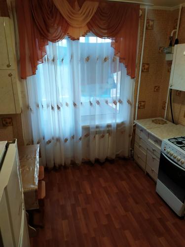eine Küche mit einem Fenster mit weißen Vorhängen und einem Herd in der Unterkunft Прокофьева 24б Уютная посуточная квартира in Sumy