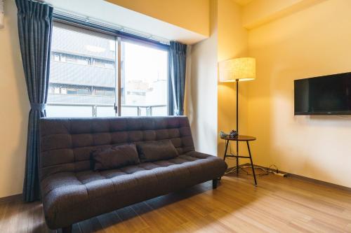 a couch in a room with a window and a television at IKIDANE Residential Hotel SHIMANOUCHI in Osaka