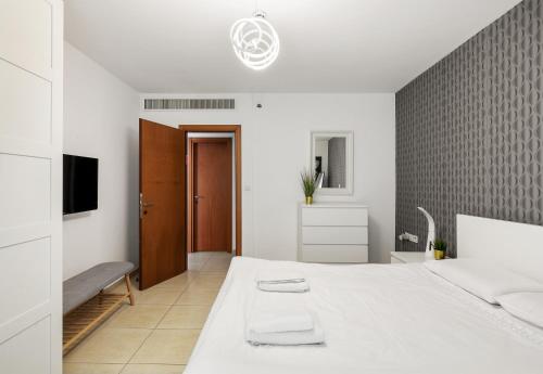 um quarto branco com uma cama e uma televisão em The Green Garden Suite by the Beach em Herzeliya