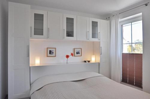 ein weißes Schlafzimmer mit einem Bett und einem Fenster in der Unterkunft Kapitänshaus 12 in Laboe