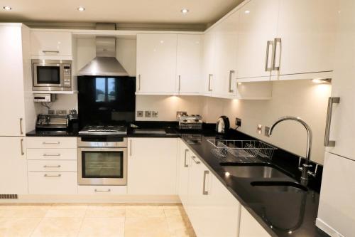 a kitchen with white cabinets and black counter tops at BEACHSIDE SPACIOUS apartment, private garden in St Merryn