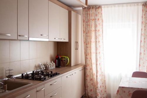 d'une cuisine avec des placards blancs, un évier et une fenêtre. dans l'établissement 21 Cozy Apartament, à Bistriţa