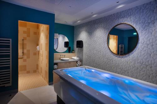 ein Badezimmer mit einer blauen Badewanne und einem Spiegel in der Unterkunft Résidence DOMITYS - L'Athénée in Mont-Saint-Aignan