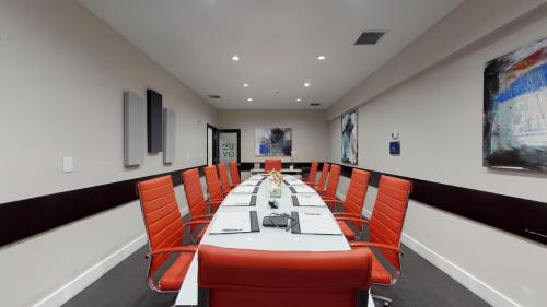 a conference room with a long table and orange chairs at Nuvo Suites Hotel - Miami Doral in Miami