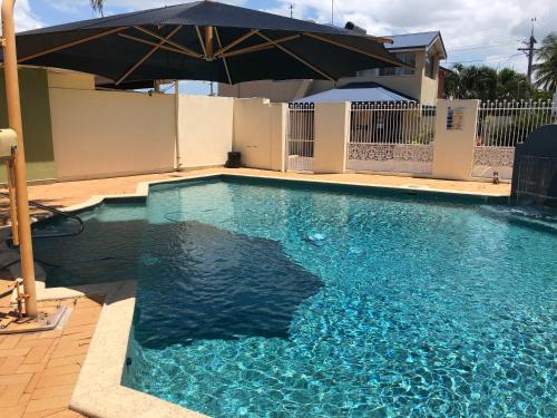 a swimming pool with an umbrella next to a house at Hervey Bay Motel in Hervey Bay