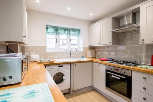 eine Küche mit weißen Schränken, einer Waschmaschine und einem Trockner in der Unterkunft 1 Roseanna Cottage, Middleton in Middleton