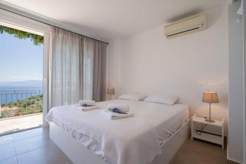 a white bedroom with a bed and a large window at Villa Koumaria in Sivota