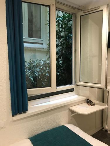 Schlafzimmer mit einem Fenster mit blauen Vorhängen und einem Bett in der Unterkunft Hotel de Bretagne in Lyon